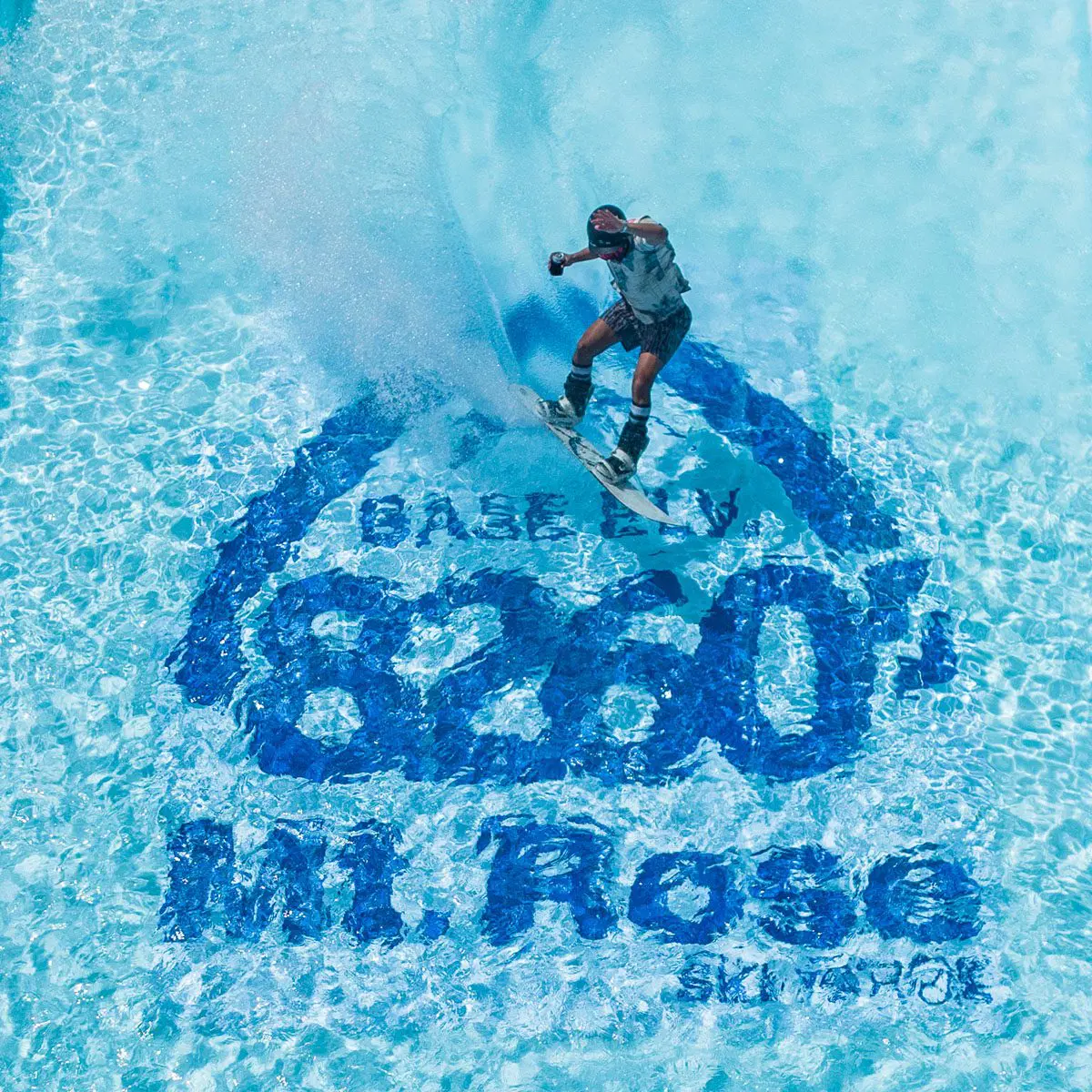 Mt. Rose A snowboarder in action skims across a pool of water at a snowy Mt. Rose Ski Tahoe Pond Skim event. The pool's bottom displays the elevation "8260" and "Mt. Rose Ski Tahoe" in large blue letters. The snowboarder creates splashes, highlighting their dynamic movement.