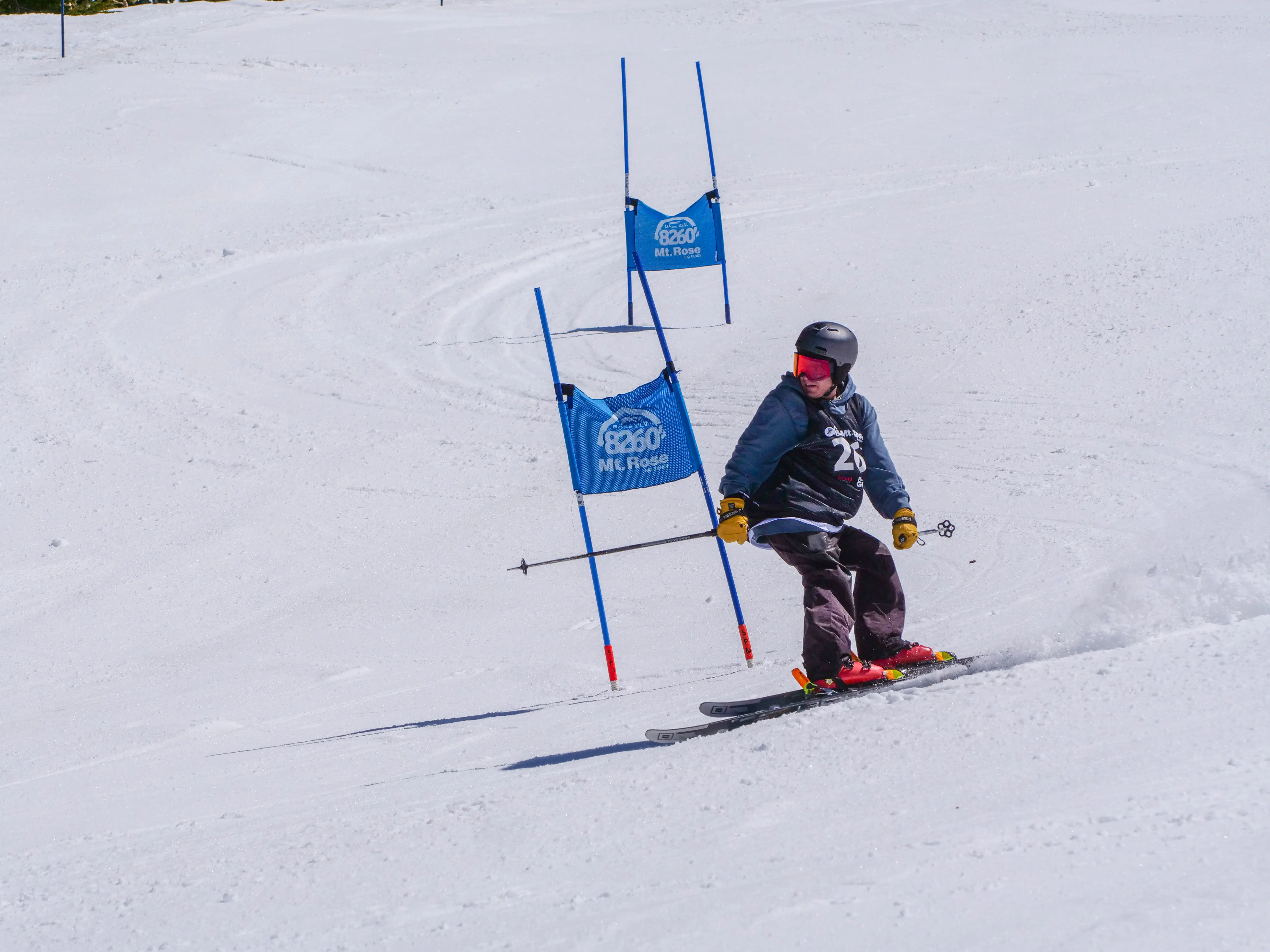 A skier wearing a helmet and goggles navigates around blue slalom gates on a snowy slope during a race. Mt. Rose Ski Tahoe