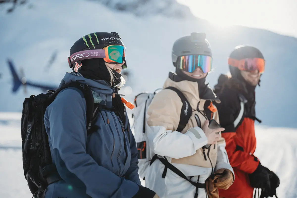 Three people in winter gear and helmets stand smiling on a snowy mountain with a helicopter and sunshine in the background, ready for a skiing or snowboarding adventure. Mt. Rose Ski Tahoe Three people in winter gear and helmets stand smiling on a snowy mountain with a helicopter and sunshine in the background, ready for a skiing or snowboarding adventure. Mt. Rose Ski Tahoe