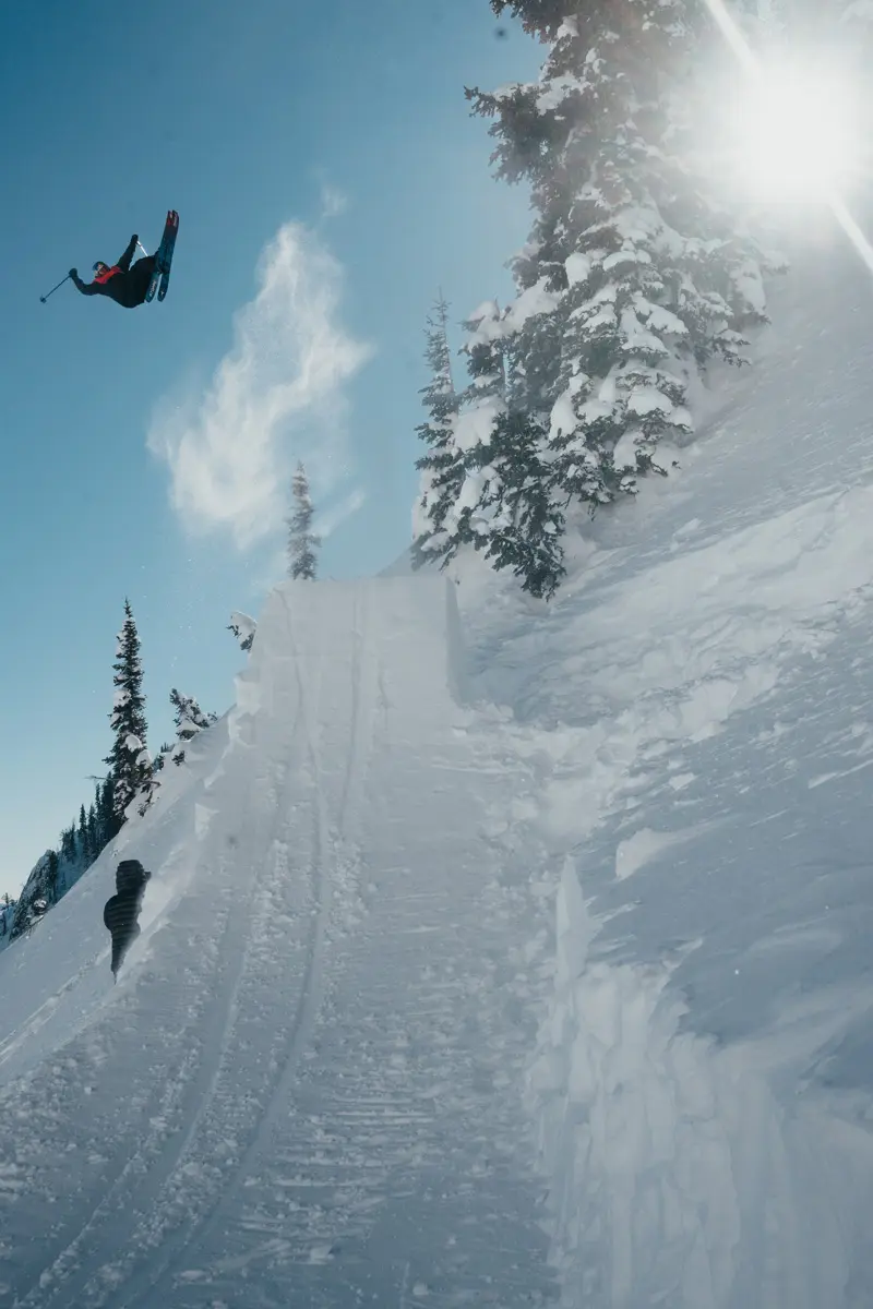 A skier performs a high jump off a snowy ramp on a mountain, with snow flying and sunlight streaming through the trees on a clear winter day. Mt. Rose Ski Tahoe A skier performs a high jump off a snowy ramp on a mountain, with snow flying and sunlight streaming through the trees on a clear winter day. Mt. Rose Ski Tahoe