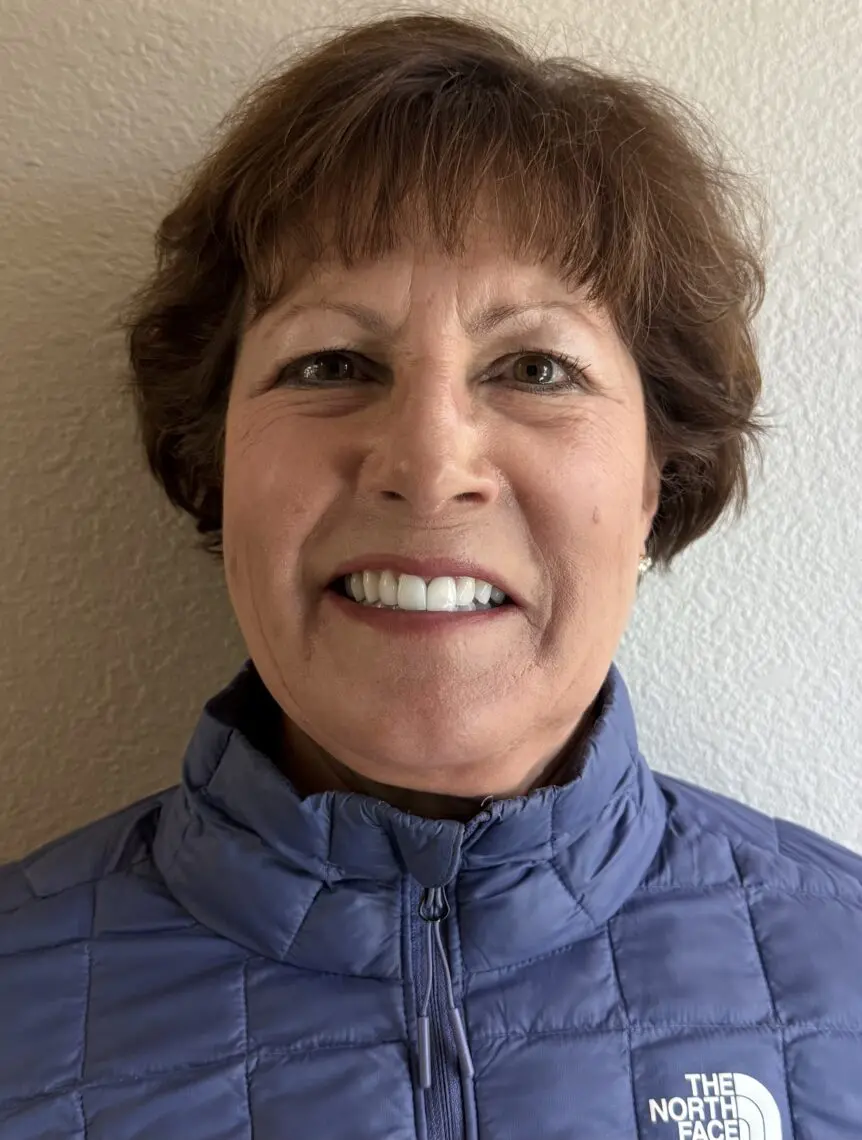 A woman with short brown hair smiles at the camera. She is wearing a blue North Face jacket and standing against a light-colored textured wall, ready to attend a film festival. Mt. Rose Ski Tahoe