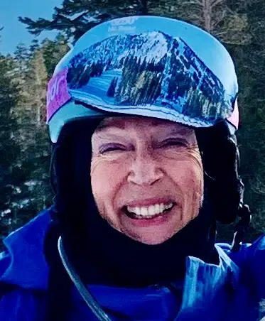 A smiling person in winter gear and a helmet stands outdoors with snowy mountains and trees—reminiscent of a film festival poster—reflected in their helmet visor. Mt. Rose Ski Tahoe