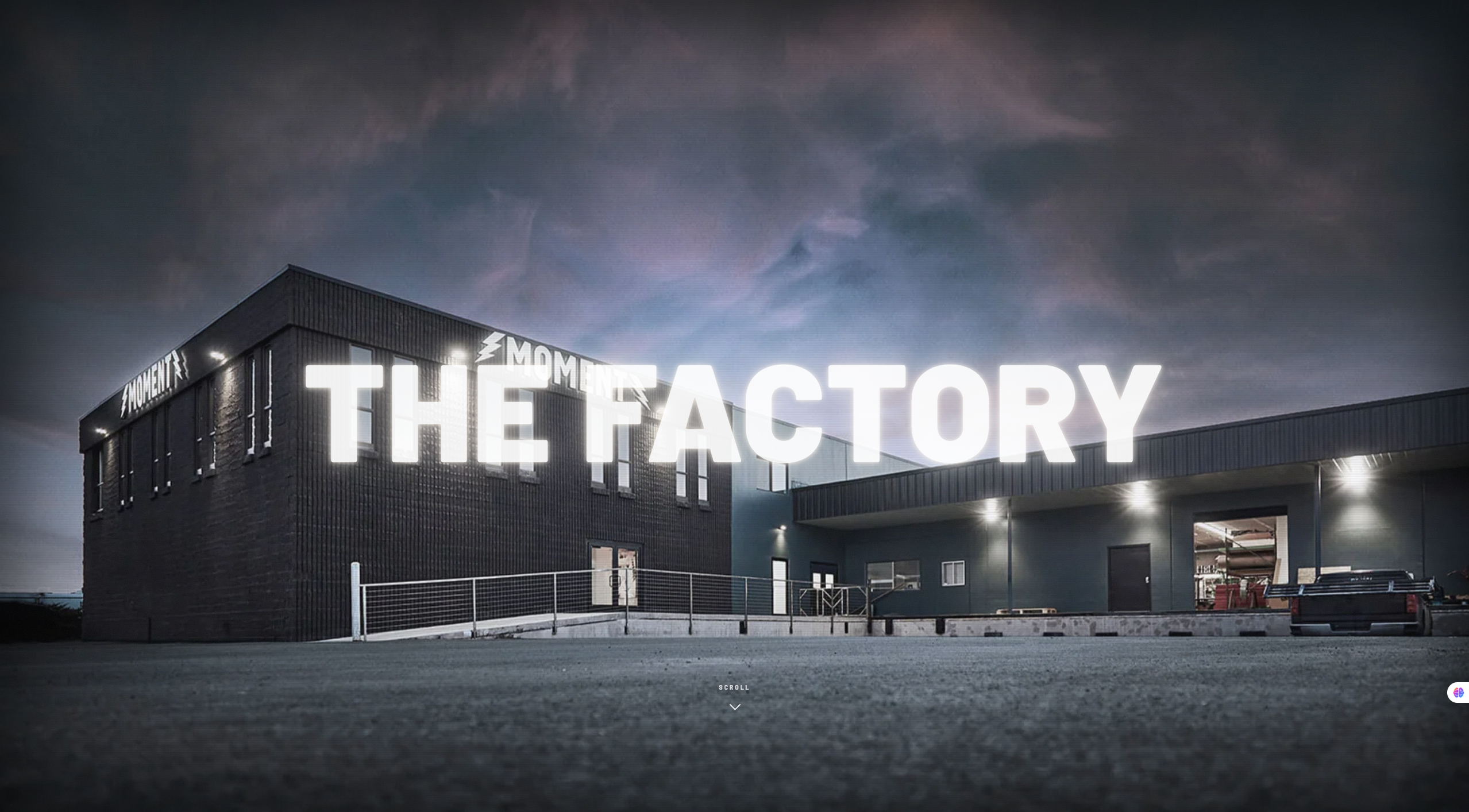 A modern factory building at dusk with large illuminated text reading “THE FACTORY” across the image. The sky is cloudy, and the ground in front appears empty—setting the stage for the upcoming Factory Kick Off Party hosted by Moment Skis. Mt. Rose Ski Tahoe