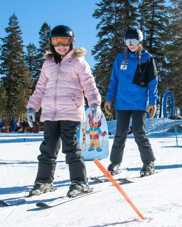 Two children in ski gear and helmets stand on skis on a snowy Ski Tahoe slope. Mt. Rose Ski Tahoe